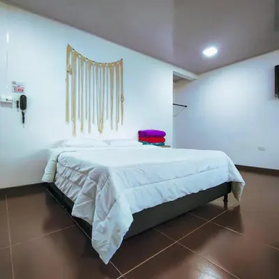 a bedroom with a white bed with a red suitcase on it at Hotel Ocaso Marinilla in Marinilla