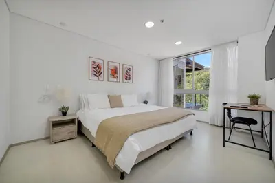 a white bedroom with a large bed and a desk at PORTANOVA Suites by ADVENTU in Rionegro