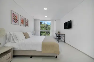 a white bedroom with a bed and a window at PORTANOVA Suites by ADVENTU in Rionegro