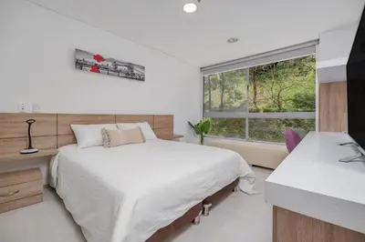 a white bedroom with a bed and a window at PORTANOVA Suites by ADVENTU in Rionegro