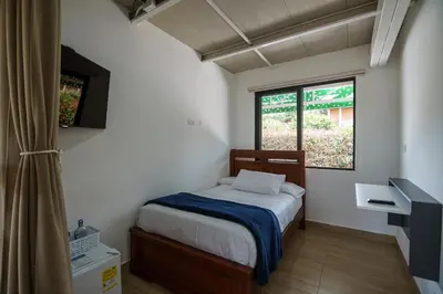 a small bedroom with a bed and two windows at Finca Hotel 12 Palmas- Aeropuerto JMC in Rionegro