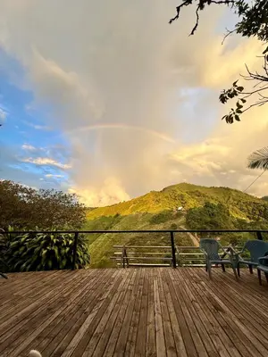 a wooden deck with two chairs and a rainbow in the sky at La Peña Cabins - Ebéjico in Ebéjico