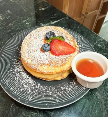 a pancake with a strawberry on a plate with a bowl of syrup at Hotel Prince Plaza - Laureles Estadio in Medellín