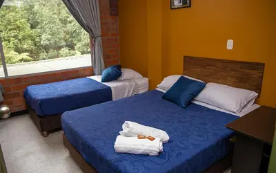 a bedroom with two beds with blue sheets and a window at Hotel Valjala in Manizales