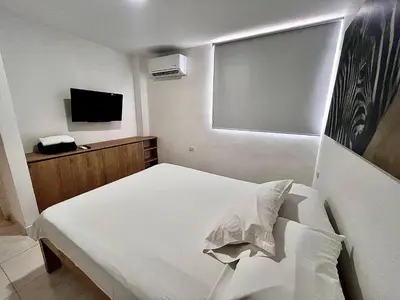 a bedroom with a white bed and a television at Apartahotel Rosedal in Doradal