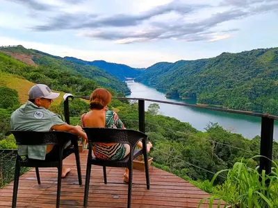 a man and woman sitting on a deck looking at a river at COCOZNA Glamping in Norcasia