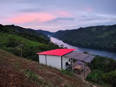 a building with a red roof on a hill next to a river at COCOZNA Glamping in Norcasia