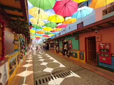 a street with colorful umbrellas hanging from the ceilings at Apto cerca Malecón, Plaza Principal, Plazoleta Zocalos, a 8 min de la Piedra del Peñol, GRATIS PARQUEADERO!!! in Guatapé