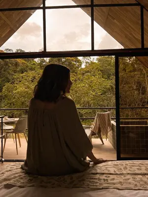 a woman sitting on a bed looking out of a window at Ceiba del Agua in San Rafael