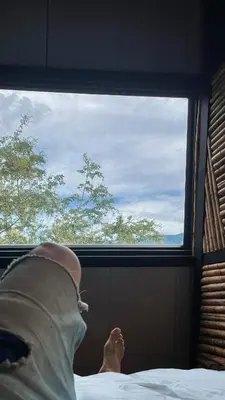 a person laying in bed looking out of a window at Cabaña 25km de Medellín, Benevento Reserva Botánica in Girardota
