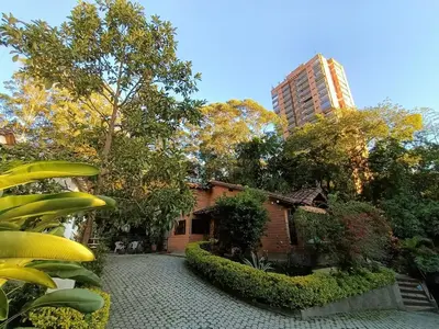a brick house with trees and a tall building at Casa Campestre 1 Nivel para 9H , Poblado San Lucas 110 in Medellín