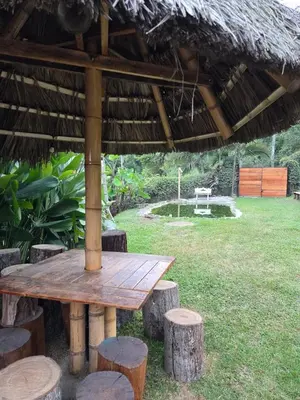 a wooden table and stools under a straw umbrella at Apartamento campestre para pareja en Manizales in Manizales