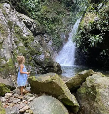 a little girl standing on rocks in front of a waterfall at Reserva Wanaka, San Carlos in Cocorná