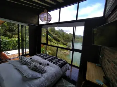 a bedroom with a bed in a room with a large window at Cabaña con jacuzzi y acceso al embalse - Portum II in El Peñol