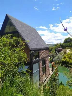 a brick house with a black roof and a river at Cabaña con jacuzzi y acceso al embalse - Portum I in El Peñol