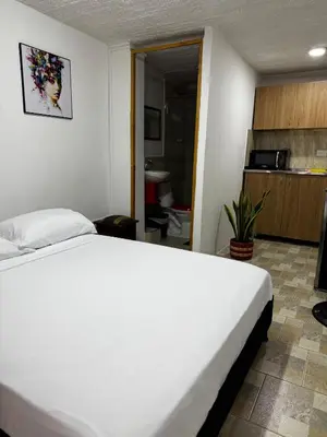 a bedroom with a white bed and a kitchen at Hermoso apartamento cerca al Poblado in Medellín
