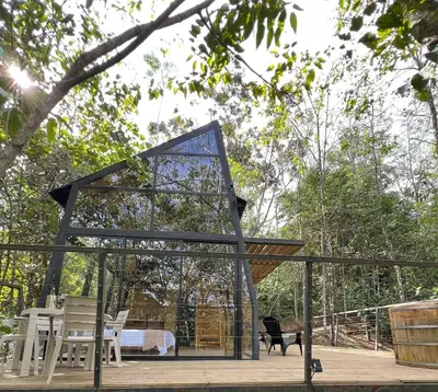 a glass pavilion with a bed and chairs on a deck at Silvery Bungalows en el Bosque in San Carlos