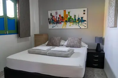 a bedroom with a bed with white sheets and a painting at Apartamento Parque Central Guatapé in Guatapé