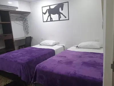 a room with two beds with purple sheets and a horse on the wall at HOTEL GANADERO in La Dorada