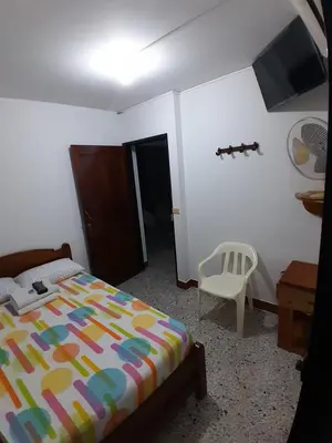 a bedroom with a bed and a white chair at Hotel Bruselas Mutata in Mutatá