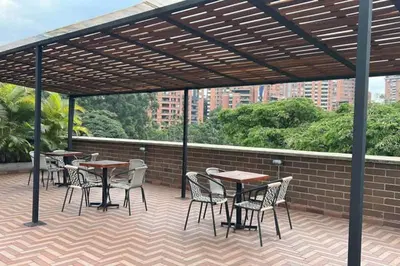 a patio with tables and chairs under a wooden pergola at Apartamentos en el Poblado Medellín - Be Together by Roots Rentals TOG APTOS in Medellín