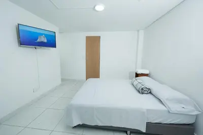 a white bedroom with a bed and a flat screen tv at Hostal Casa Host 72 in Medellín