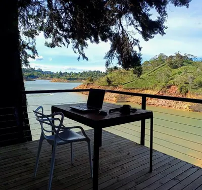 a table and chair on a deck with a laptop at Tree House, Cabaña privada con Jacuzzi y canoa in Guatapé