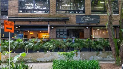 a restaurant with palm trees in front of a building at Dormitorios en Medellín con áreas comunes, Coworking - Be Together by Roots Rentals TOG HAB in Medellín