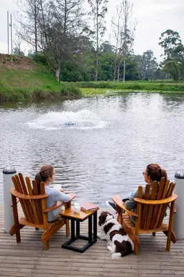 two women sitting in chairs next to a body of water at Monarch Campestre- Rionegro in Rionegro