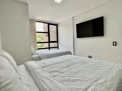 a white bedroom with a bed and a flat screen tv at 802, Amazing apartment in heart of El Poblado + View! in Medellín
