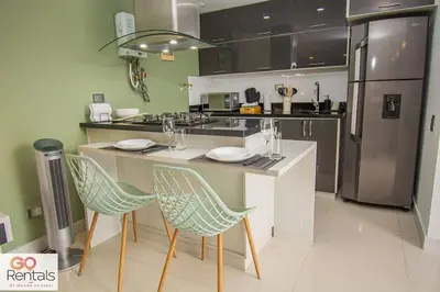 a kitchen with a counter with chairs and a refrigerator at Cozy studio in Poblado, parking, NO FEE 1107 in Medellín