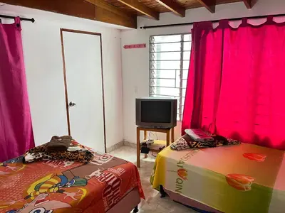 two beds in a room with pink curtains and a tv at Hostal Monarca in Medellín