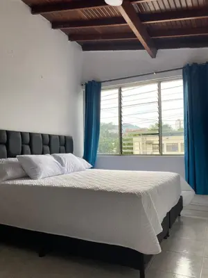 a bedroom with a bed with blue curtains and a window at Hotel Mallorca Estadio, Medellin in Medellín