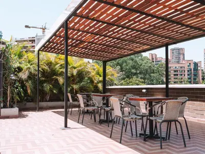 a patio with tables and chairs under a wooden pergola at Económicas habitaciones amobladas en Medellín con oficinas, puesto de trabajo, cocina, baño y lavandería comunes Be Together by Roots Rentals TOG401y402 in Medellín