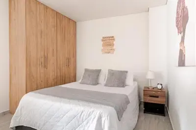 a white bedroom with a bed and a wooden cabinet at Apartamento centro Marinilla in Marinilla