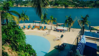 a swimming pool next to a beach with a body of water at Viajero Guatapé Hostel & Lake Club in Guatapé