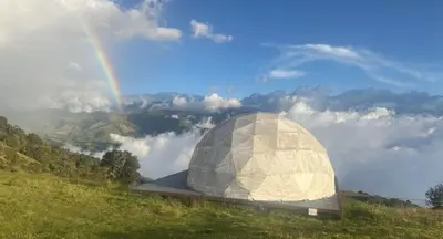 a dome building on a hill with a rainbow in the background at Fabrica de Rios Glamping in Manizales