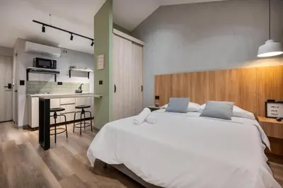 a bedroom with a large white bed and a kitchen at Casa Origo Hospedaje in Medellín