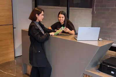 two women standing at a desk with a laptop at Cozy Comfort at Rosa Negra Stadio Suite in Medellín
