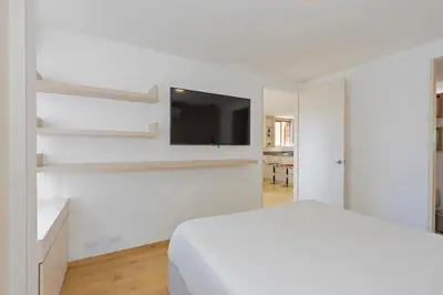 a white bedroom with a bed and a flat screen tv at Alcazar de oviedo by Host Medellin in Medellín