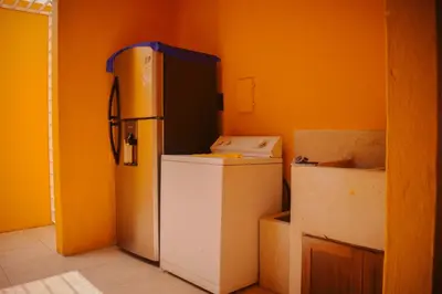 a kitchen with an orange wall with a refrigerator at Villas Mamilú, entrada y salida 100 por ciento flexible in Santa Fe de Antioquia