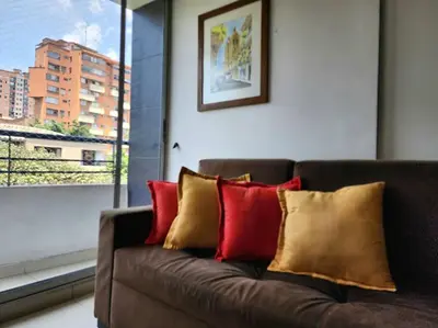 a brown couch with red and yellow pillows next to a window at Vivienda Céntrica y Acogedora in Sabaneta