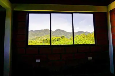 a window in a brick wall with a view of mountains at Retro Finca Urrao - Peaceful Avocado Farm Retreat in Urrao