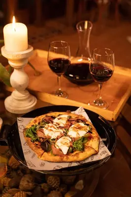 a pizza on a plate on a table with glasses of wine at LasNubes EcolodgeNubes Ecolodge in Santa Elena