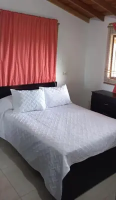 a bedroom with a white bed with a red curtain at Casa de campo in Jericó