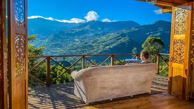 a woman sitting in a wicker chair on a balcony with a view of mountains at Finca Milena Jardin Antioquía in La Morelia