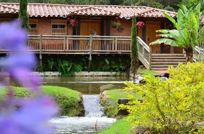a house with a river in front of a building at Refugio Natural - Cabañas Ecológicas con Jacuzzi, Guarne in Guarne