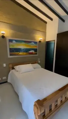 a bedroom with a large white bed with a painting on the wall at Hermosa Cabaña Familiar in San Jerónimo