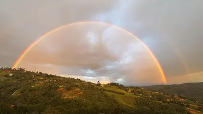 a rainbow in the sky over a hill at Cabaña Del bosque in Santa Elena