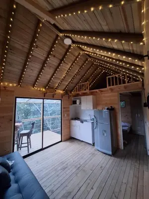 a living room with a couch and a kitchen with lights at Cabaña Del bosque in Santa Elena